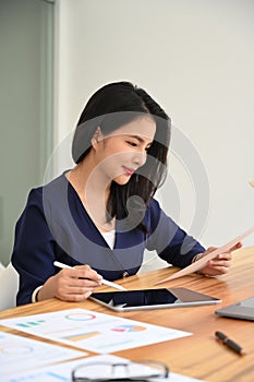 Portrait of female manager holding document and using digital tablet at wooden office