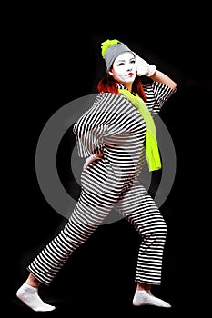 Portrait of female mime artist, isolated on black background. Young woman in striped suit and bright yellow scarf and