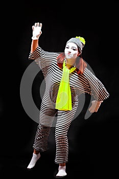 Portrait of female mime artist, isolated on black background. Young woman in striped suit and bright yellow scarf and