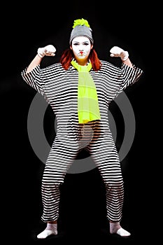 Portrait of female mime artist, isolated on black background. Young woman in striped suit and bright yellow scarf and