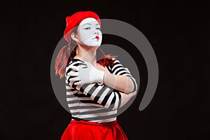 Portrait of female mime artist performing, isolated on black background. Woman in striped clothes and red skirt is