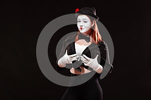 Portrait of female mime artist performing, isolated on black background. Woman touches her breast with confident look