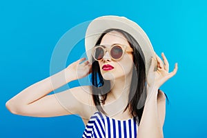 Portrait of Female Model in Fashion Sunglasses and Summer Hat on Blue Background.