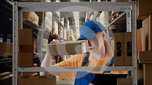 Portrait of female model working in storage. Girl storekeeper in uniform standing near rack with boxes, checks goods