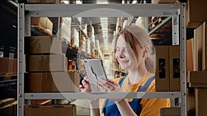 Portrait of female model working in storage. Girl storekeeper in uniform standing near rack with boxes, watching social