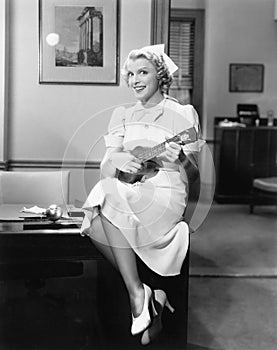 Portrait of a female nurse sitting on a table and playing a guitar