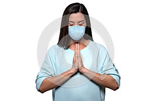 Portrait of a female nurse in surgical mask keeping calm during world pandemic scare, praying hands isolated on white background