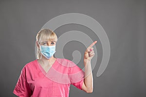 Portrait of female nurse wearing face mask pointing copy space