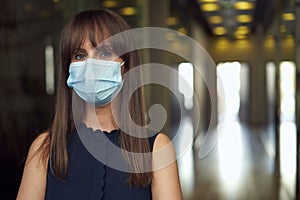 Portrait of female office worker in office building hallway, wearing face mask