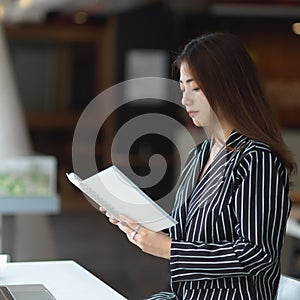 Female office worker reading her schedule book while sitting in office room