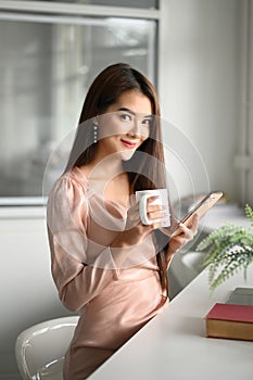 Portrait of female office worker relaxed and sitting at worktable with coffee cup.