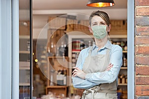 Portrait Of Female Owner Standing Outside Delicatessen Wearing Face Mask During Health Pandemic