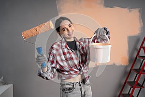 Portrait on female painter showing bucket and painting roller on the camera. Woman renovation her new house