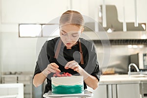 Portrait of a female pastry chef who is decorating a cake with fresh berries.