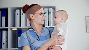 portrait of a female pediatrician holding a small child in her arms in a medical office, smiling and looking at camera