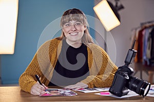 Portrait Of Female Photographer At Desk Checking Brief Before Fashion Shoot In Studio