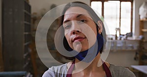 Portrait of female potter with lowered face mask at pottery studio