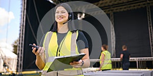 Portrait Of Female Production Worker Setting Up Outdoor Stage For Music Festival Or Concert