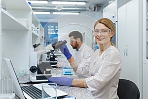 Portrait of female scientist laboratory assistant, researcher working inside medical laboratory with microscope, looking