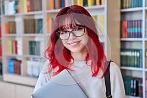 Portrait of female college student in glasses with laptop backpack, looking at camera