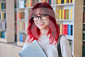 Portrait of female college student in glasses with laptop backpack, looking at camera