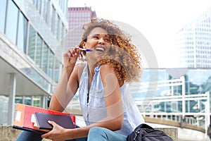 Female student laughing outside with pen and books photo