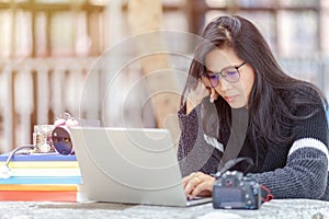 Portrait of female student sitting at the park and using laptop , writing thesis with serious face expression.