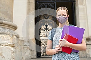 Portrait Of Female Student Standing Outside College Or University Building Wearing Face Mask During Covid-19 Pandemic