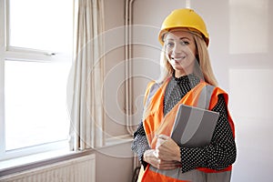 Portrait Of Female Surveyor In Hard Hat And High Visibility Jacket With Digital Tablet Carrying Out House Inspection