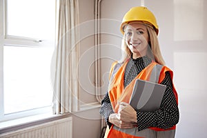 Portrait Of Female Surveyor In Hard Hat And High Visibility Jacket With Digital Tablet Carrying Out House Inspection photo