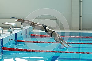 Portrait of a female swimmer, that jumping and diving into indoor sport swimming pool.