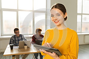 Portrait of female team leader businesswoman standing in office with colleagues meeting in background. Smiling confident