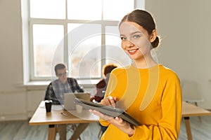 Portrait of female team leader businesswoman standing in office with colleagues meeting in background. Smiling confident