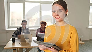 Portrait of female team leader businesswoman standing in office with colleagues meeting in background. Smiling confident