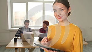 Portrait of female team leader businesswoman standing in office with colleagues meeting in background. Smiling confident