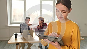 Portrait of female team leader businesswoman standing in office with colleagues meeting in background. Smiling confident