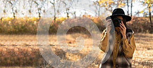 Portrait of female tourist photographer taking photo of autumn forest. Travel and hobby concept. Banner.