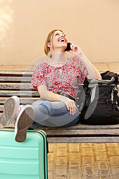 Female traveler with luggage sitting on bench and talking on cellphone