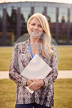 Portrait Of Female University Or College Tutor Outdoors With Modern Campus Building In Background