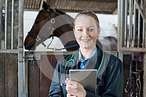 Portrait Of Female Vet With Digital Tablet Examining Horse In St