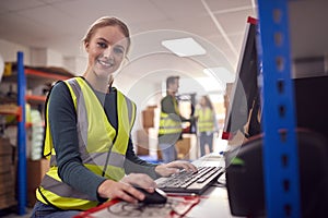 Portrait Of Female Worker In Busy Modern Warehouse Working On Computer Terminal