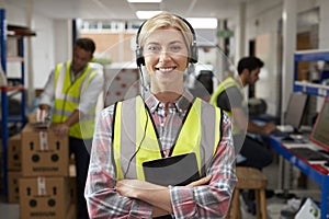 Portrait Of Female Worker Using Headset In Distribution Warehouse With Digital Tablet