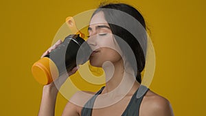 Portrait female in yellow studio drinking water enjoy hydration ethnic Indian strong sporty girl with bottle refreshment