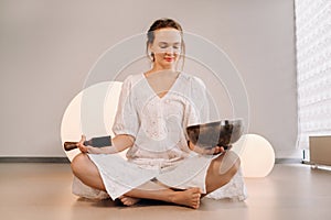 Portrait of a female yoga teacher playing a Tibetan bowl or singing a bell in the gym during a yoga retreat