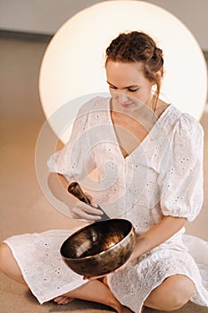 Portrait of a female yoga teacher playing a Tibetan bowl or singing a bell in the gym during a yoga retreat