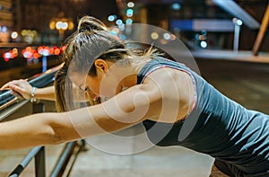 Portrait of female young athlete resting over banister after training at night in the city.