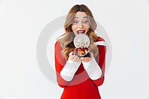 Portrait of festive woman 20s wearing Santa Claus red costume smiling and holding Christmas snow ball, isolated over white