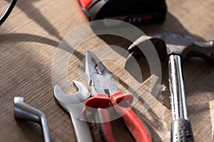 A portrait of a few tools lying on a wooden table. There are  pliers, an open and box end wrench and a claw hammer on it waiting