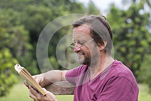 Portrait of fifty years old caucasian man reading a book outdoor in a park during a sunny summer day