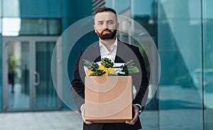 Portrait of fired upset desperate businessman in suit standing outdoors with box of stuff. Male office worker lost job